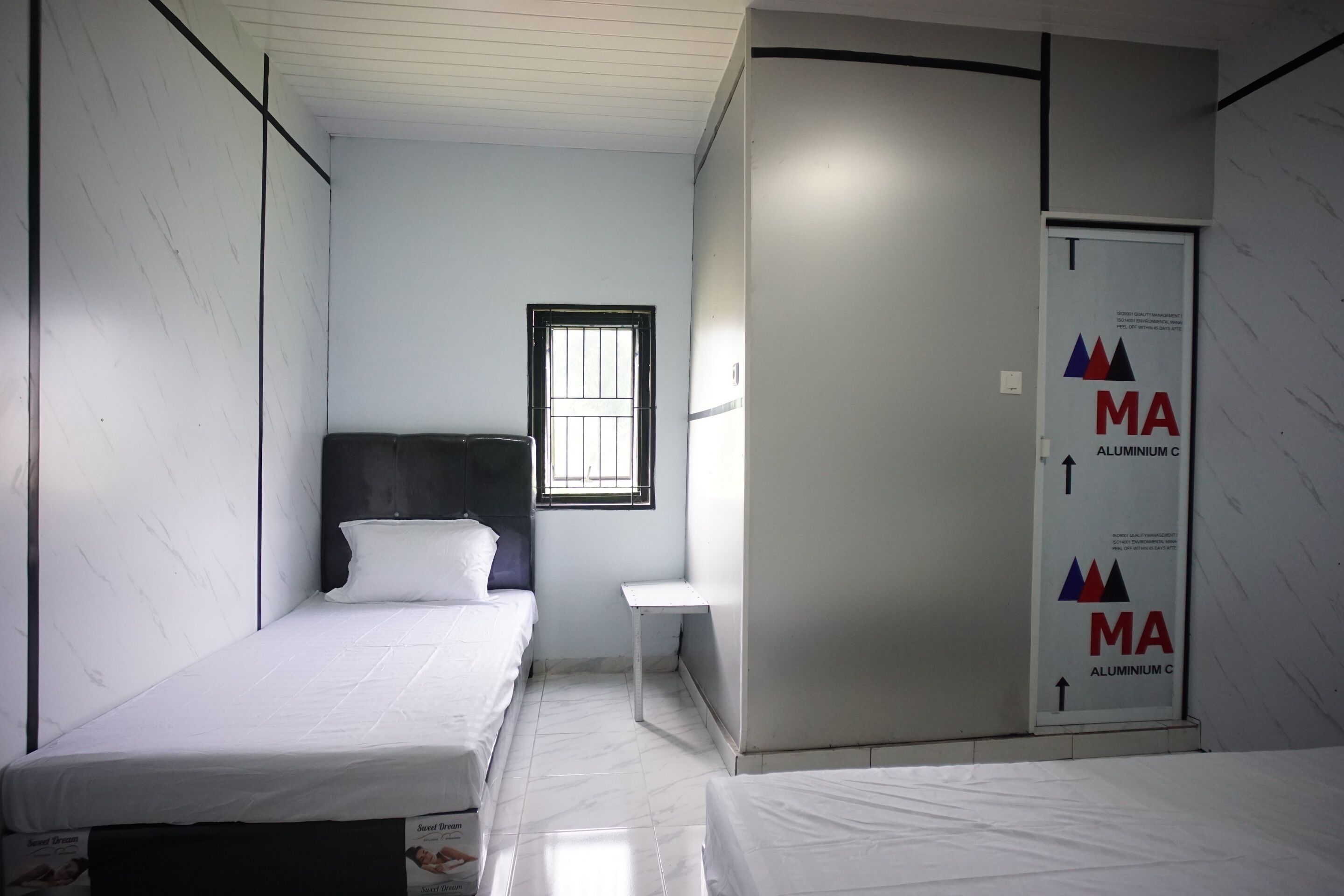 A room with two single beds, a small table, a window, and a door with a company logo.