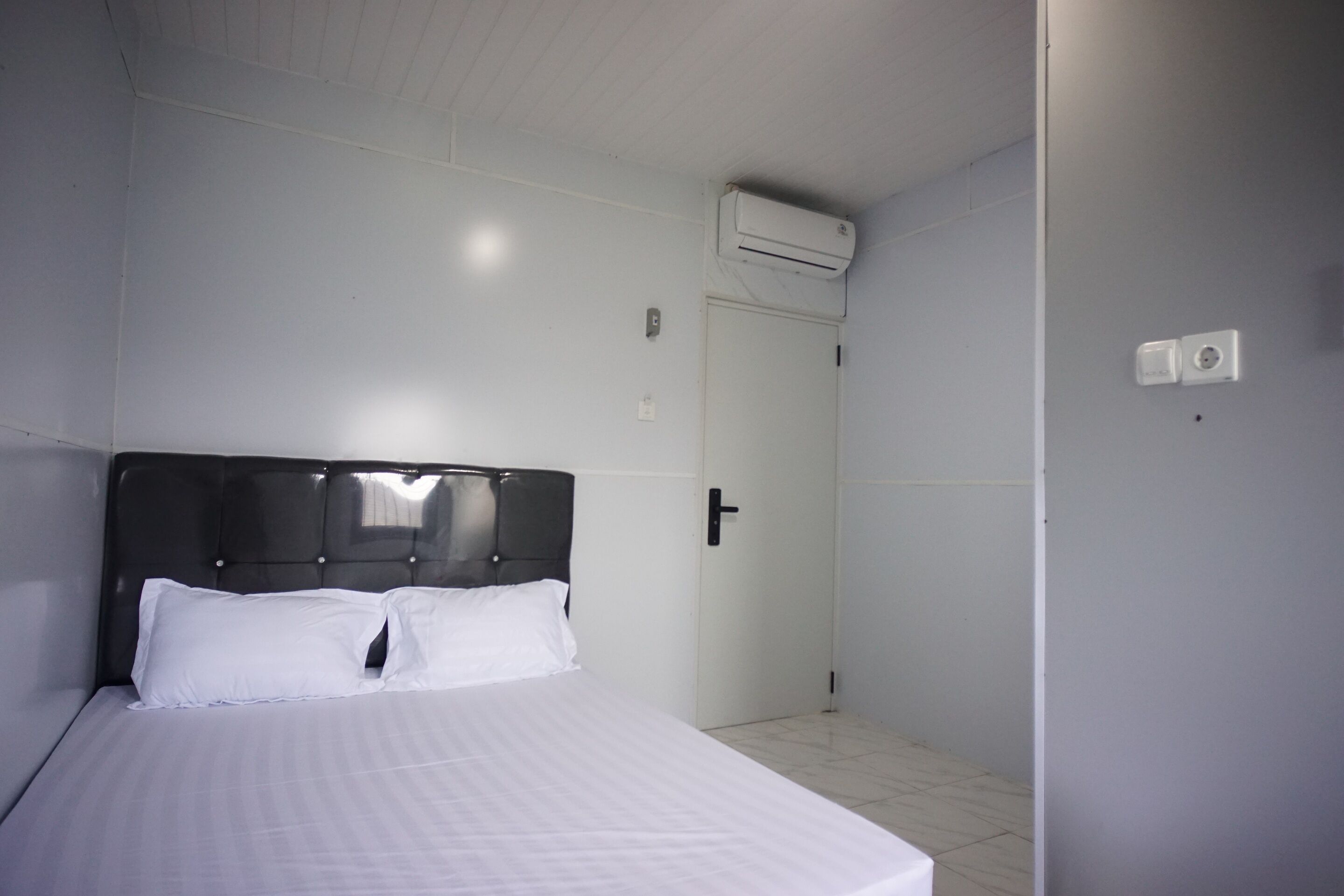 Un dormitorio con cama, una puerta y equipo de aire acondicionado.