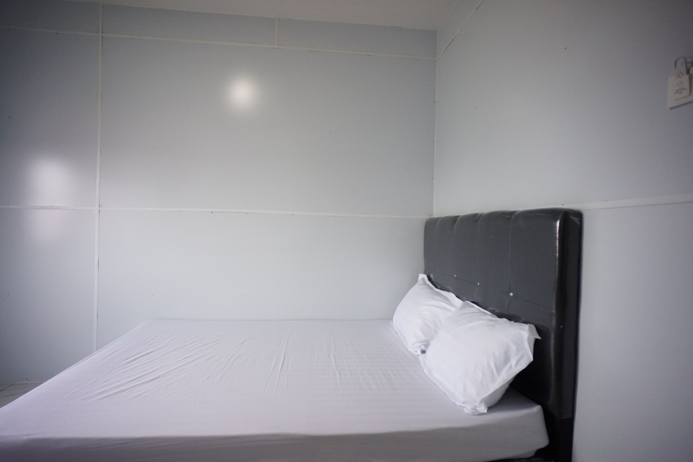 A single bed with a dark headboard in a room with white tiled walls.