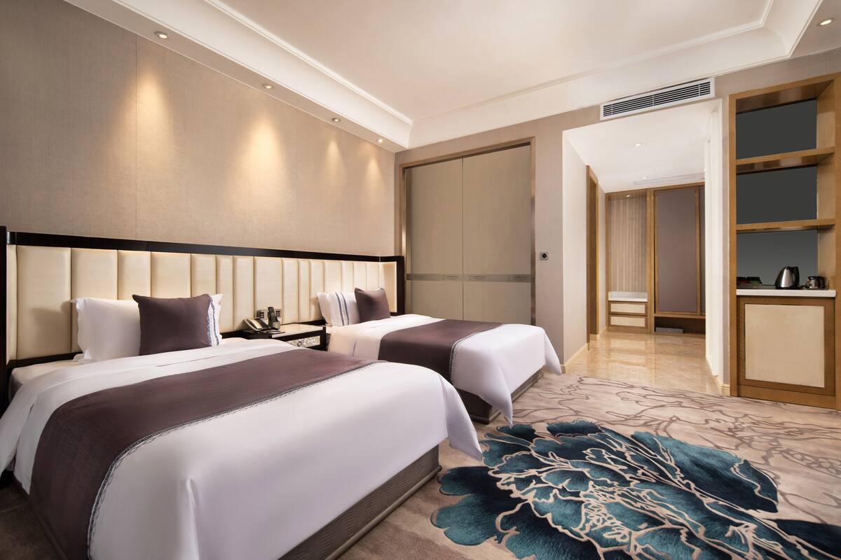 Habitación de hotel con dos camas, un espejo grande, un armario y una pequeña cocina.