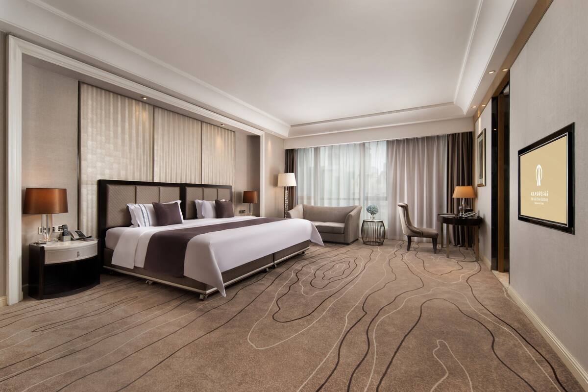 Una habitación de hotel con una cama grande, un escritorio, una silla y una mesita de noche con lámpara.