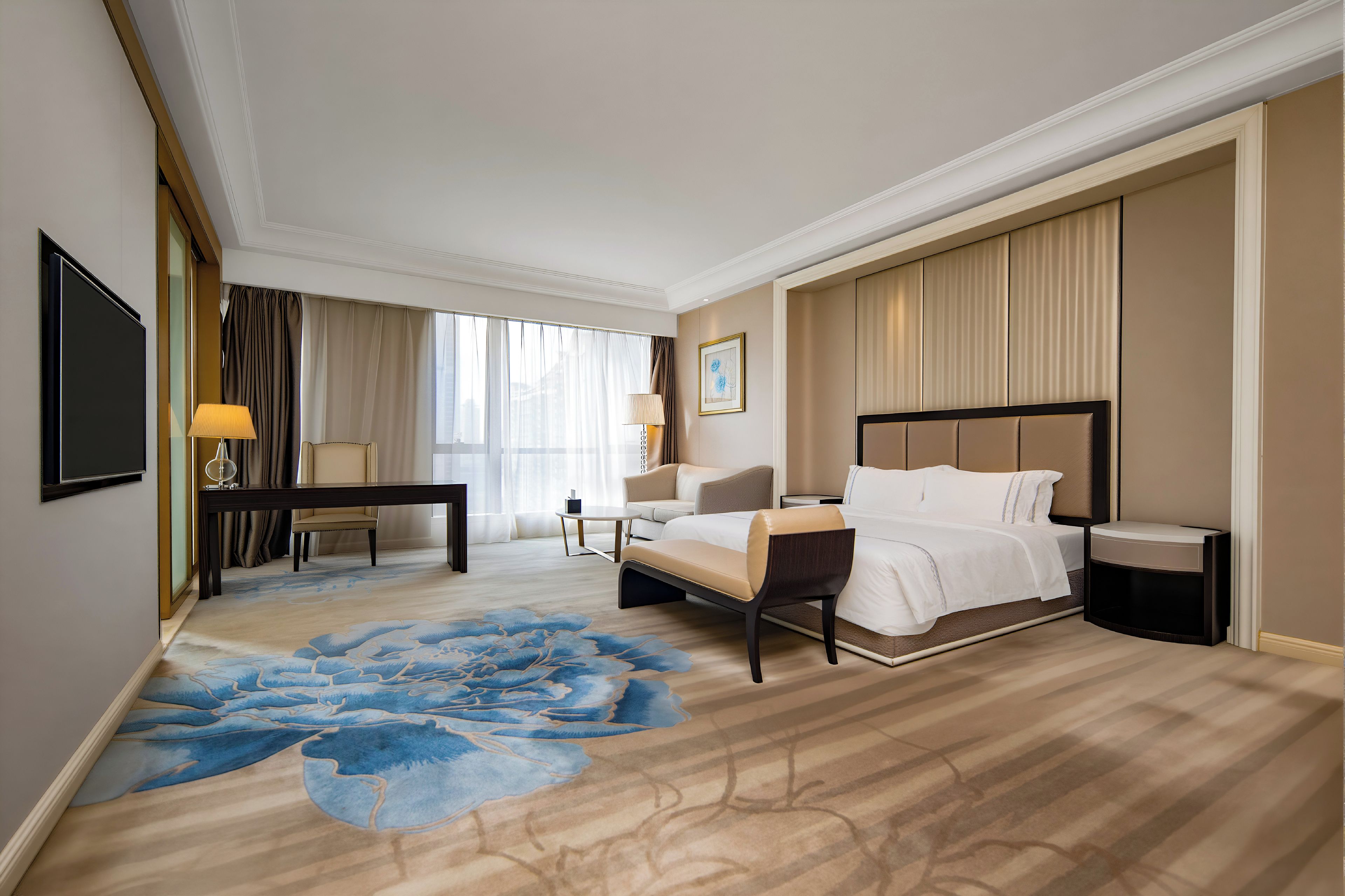 Una camera d'hotel con un letto, comodini, una scrivania, una sedia, un'ampia finestra con tende e un tappeto blu con motivi floreali.