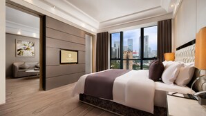 Ein modernes Hotelzimmer mit einem großen Bett, einer Couch, einem Fernseher und Blick auf die Stadt.