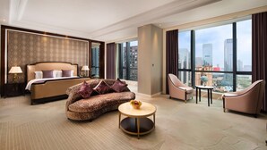 Ein modernes Hotelzimmer mit einem großen Bett, einer Couch, einem Couchtisch und Blick auf die Skyline.