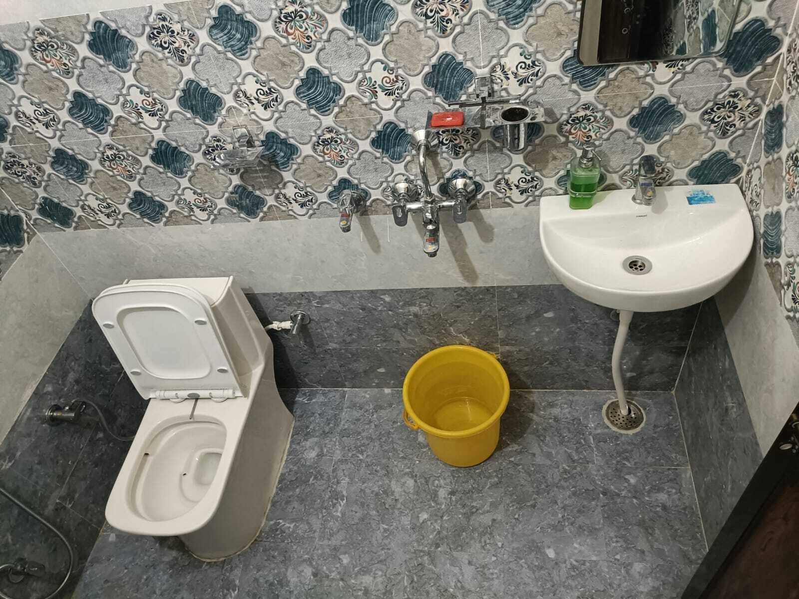 A bathroom with a toilet, a sink, and a yellow bucket on the floor.