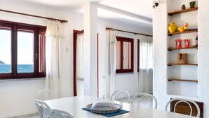 Un comedor con una mesa, sillas, vajilla de vidrio, vistas al mar y un estante con objetos.