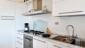 Een moderne keuken met witte kastjes, een roestvrijstalen spoelbak, een gasfornuis en een ingebouwde oven.