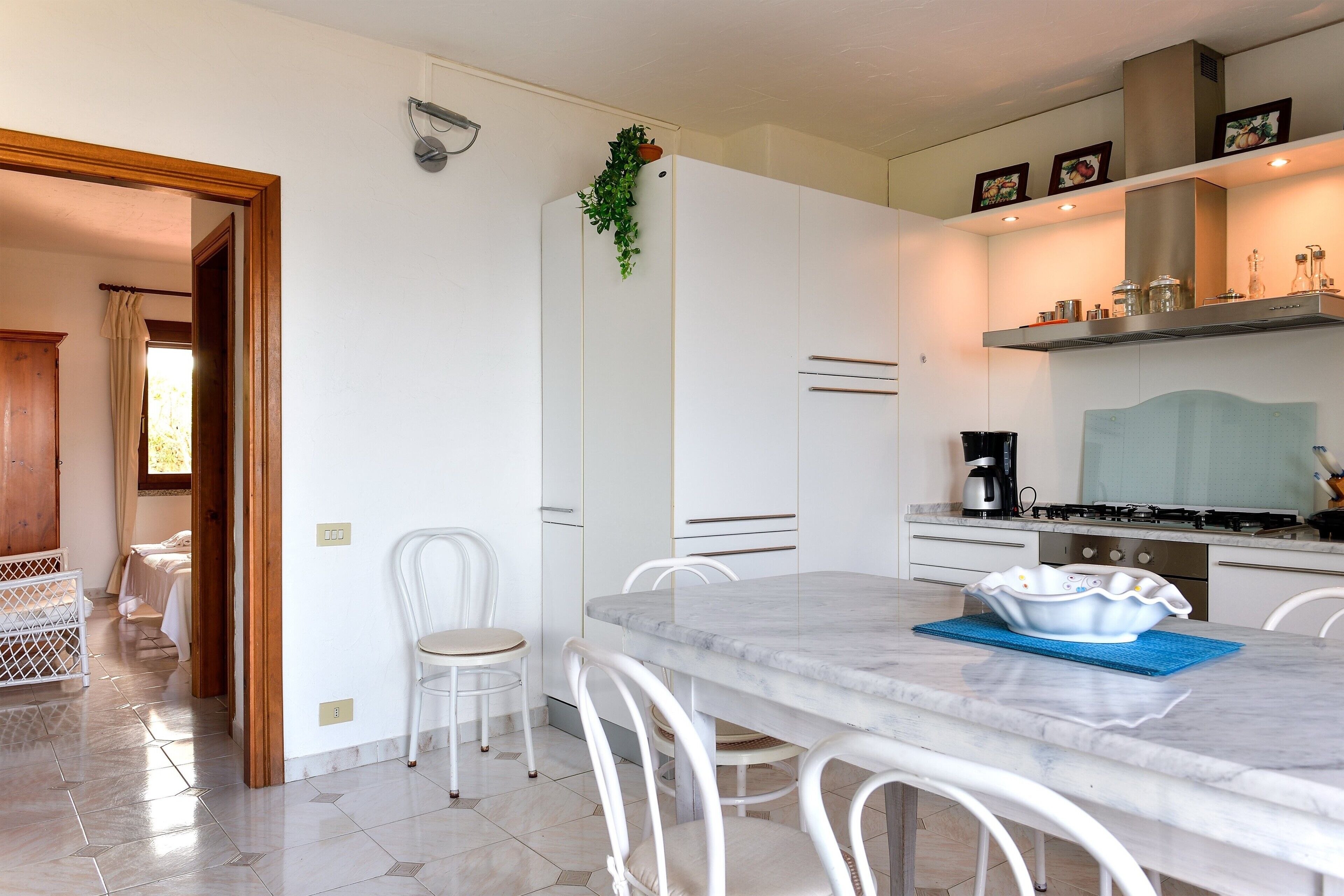 Een moderne keuken met witte kastjes, een marmeren aanrecht en een eethoek met witte stoelen.