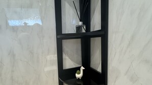 A corner shelf unit with a white ceramic pig figurine, a small potted plant, and a reed diffuser.