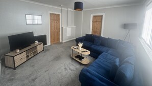 A living room with a blue sofa, a TV, a wooden cabinet, and a ceiling fan.