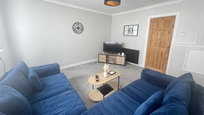 A living room with a blue sofa set, a wooden coffee table, a television, and a clock on the wall.