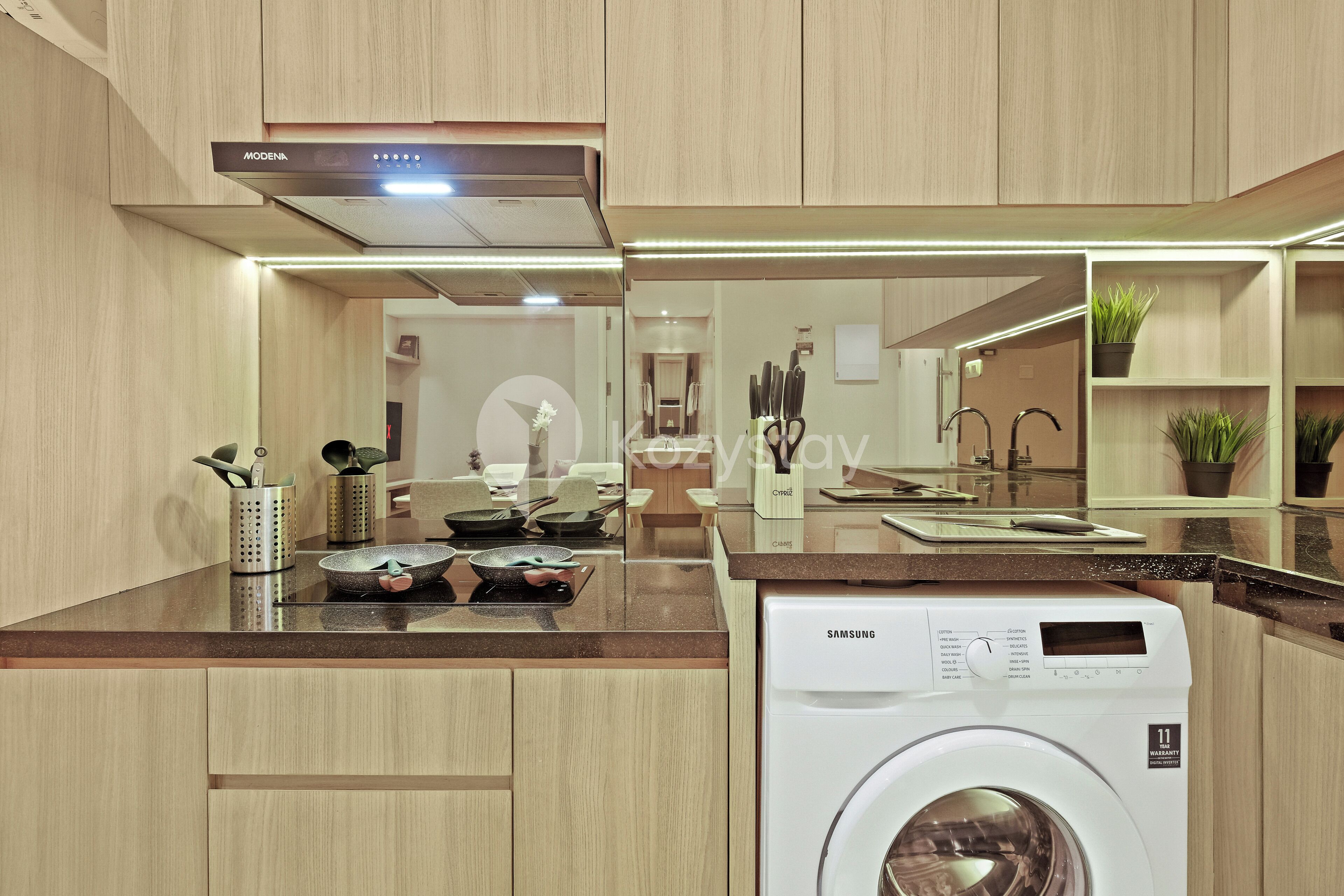 Una cocina moderna con armarios de madera, lavadora integrada y encimera con utensilios de cocina.