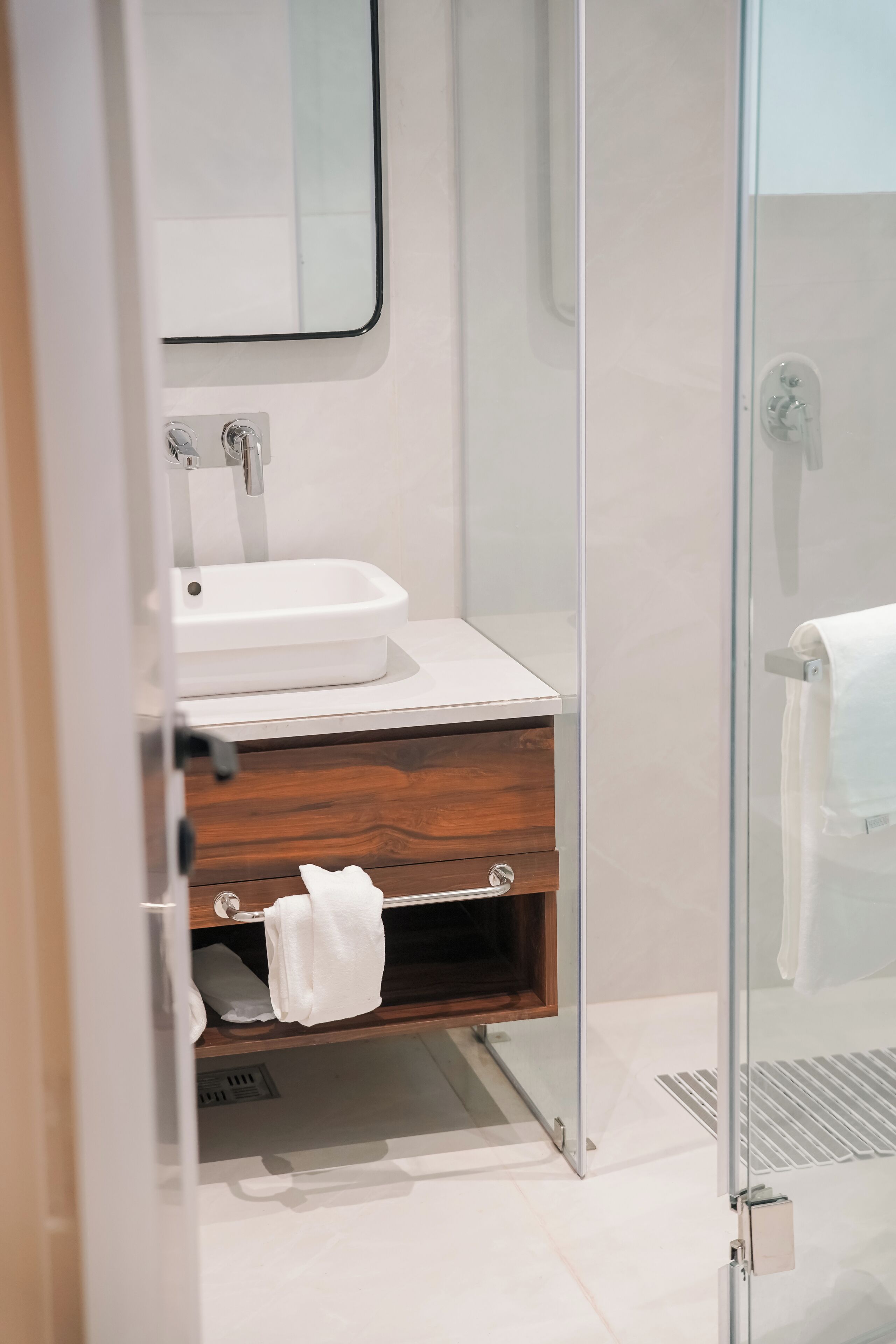 Un baño moderno con cabina de ducha de vidrio, un lavabo blanco y un mueble de tocador de madera.
