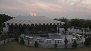 A covered outdoor seating area with tables and chairs, a central circular seating area, and a sign that reads "SPRING." - KMR Hotels & Resorts (Bikaner)