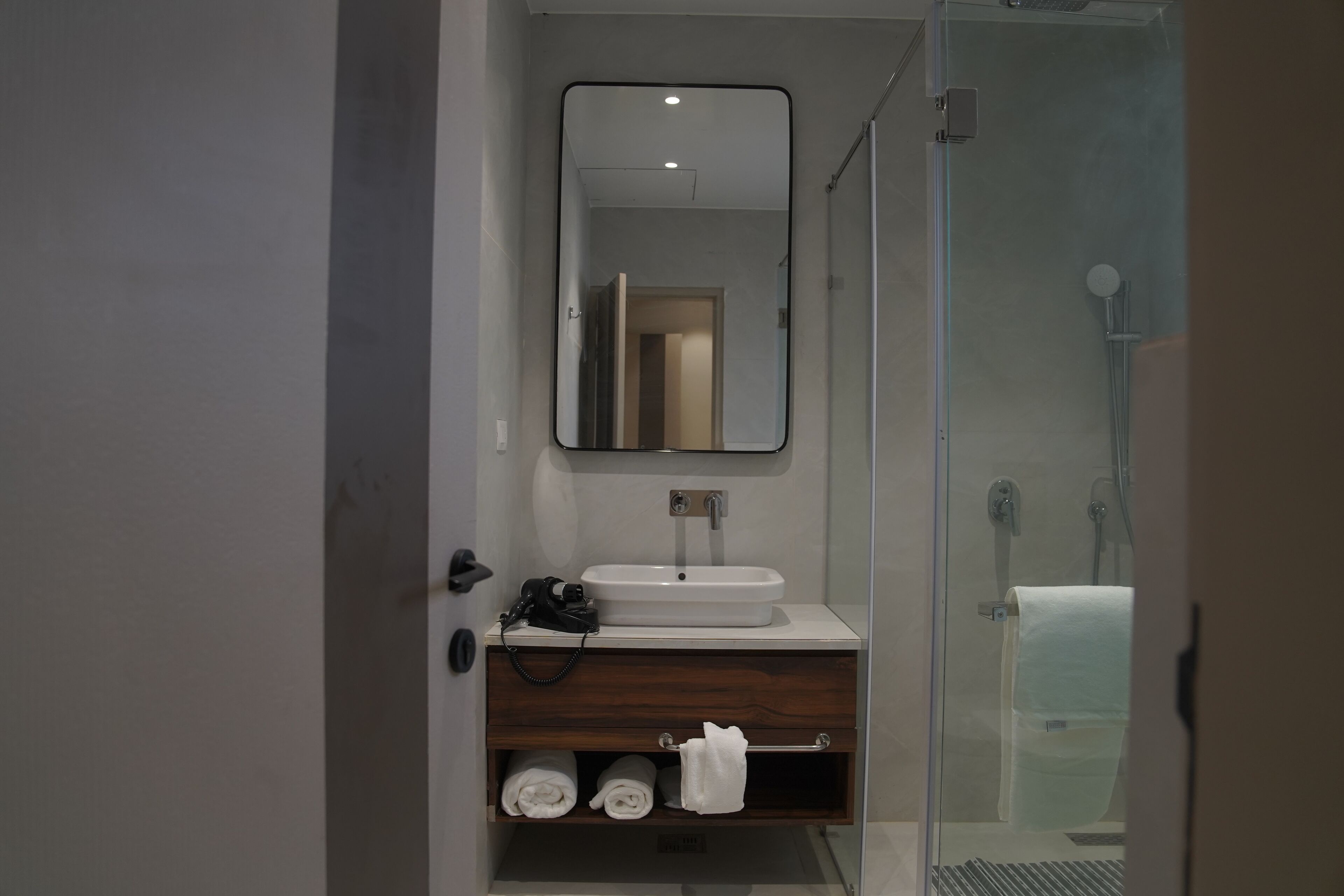 A modern bathroom with a glass shower enclosure, a white sink, and a wooden vanity.