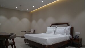A modern bedroom with a wooden bed, bedside tables, a desk, and a chair. - KMR Hotels & Resorts (Bikaner)