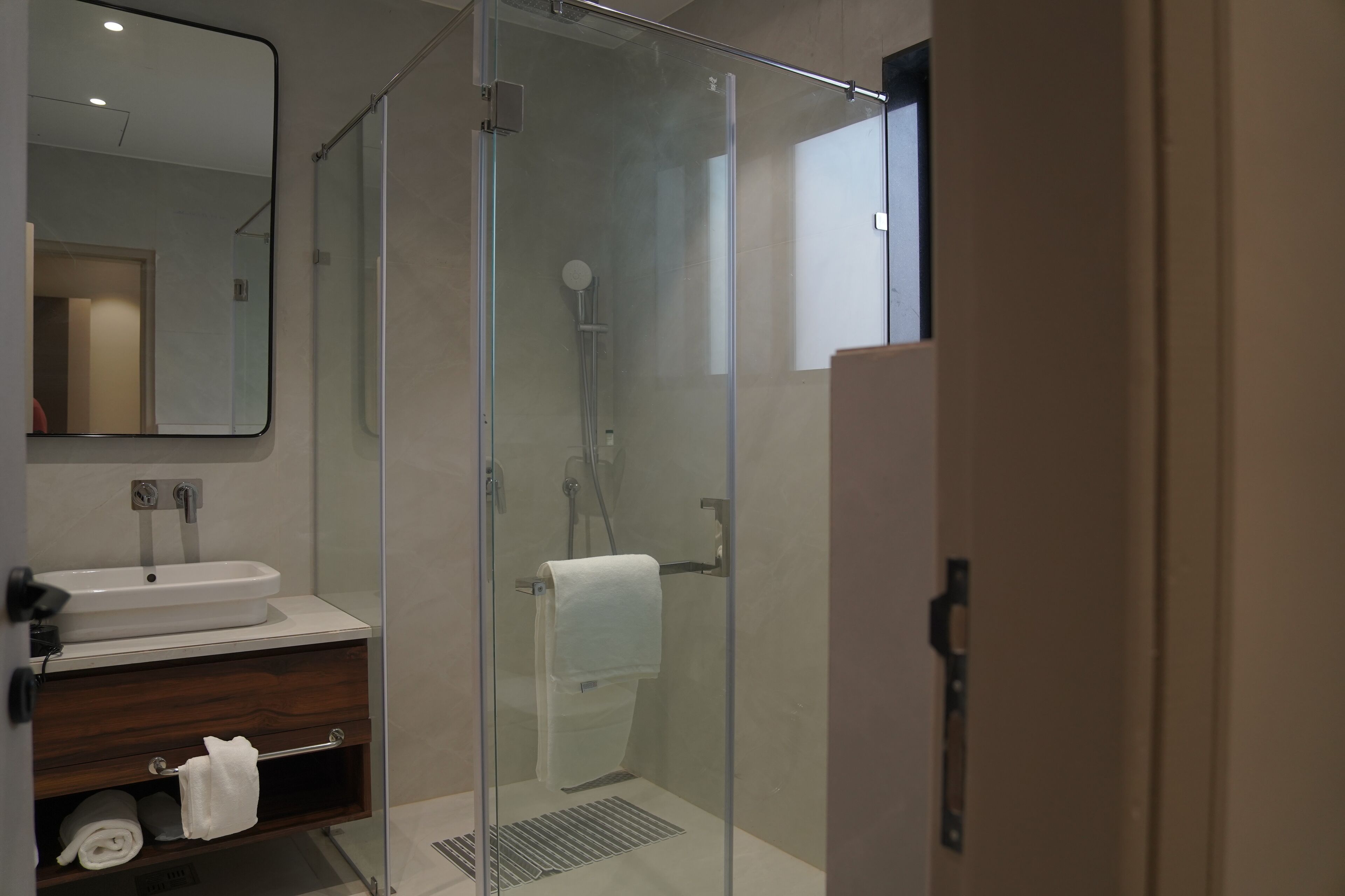 Une salle de bain moderne avec une douche à parois de verre, un lavabo blanc et un meuble-lavabo en bois.