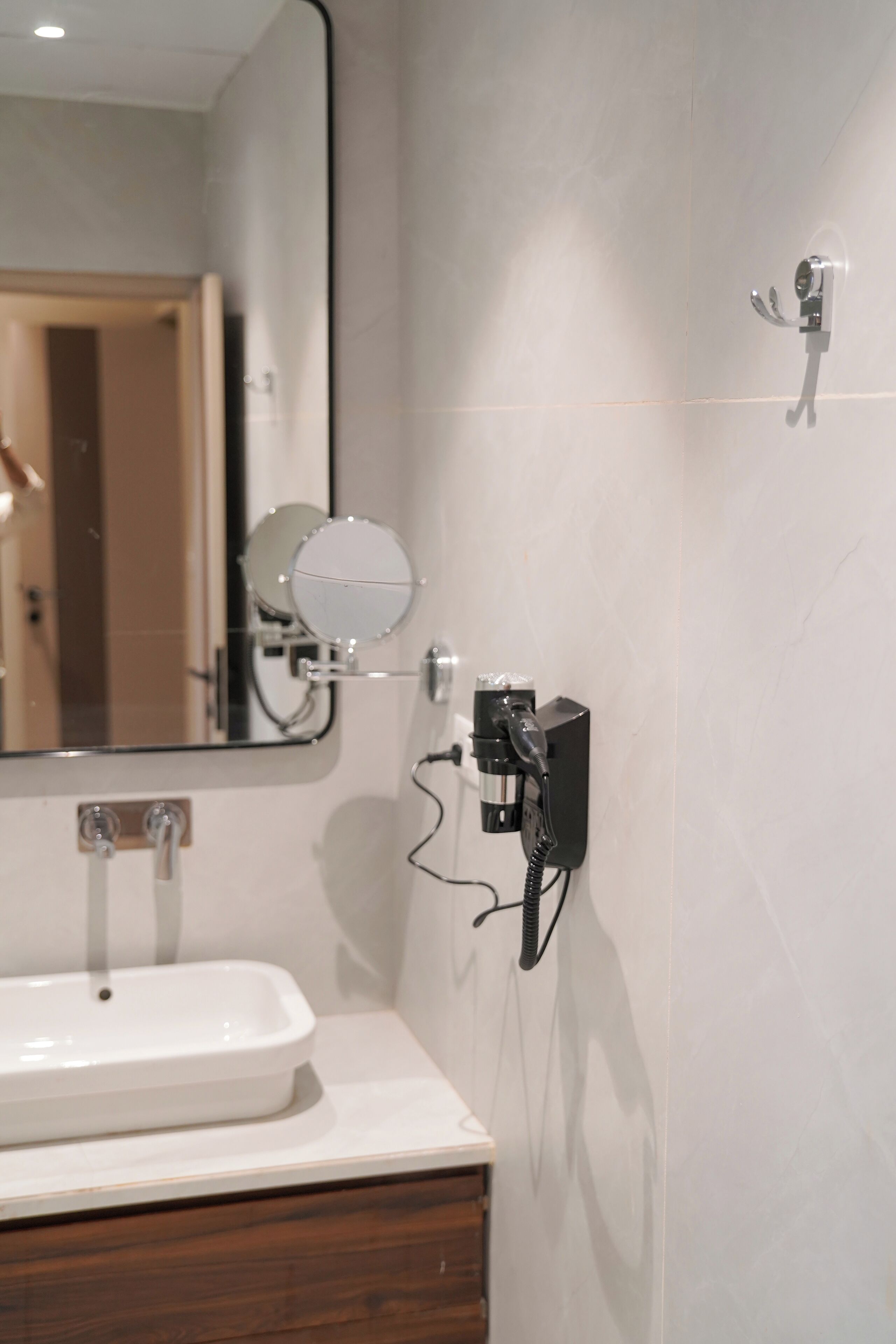 A bathroom with a white sink, a mirror, and a hairdryer mounted on the wall.