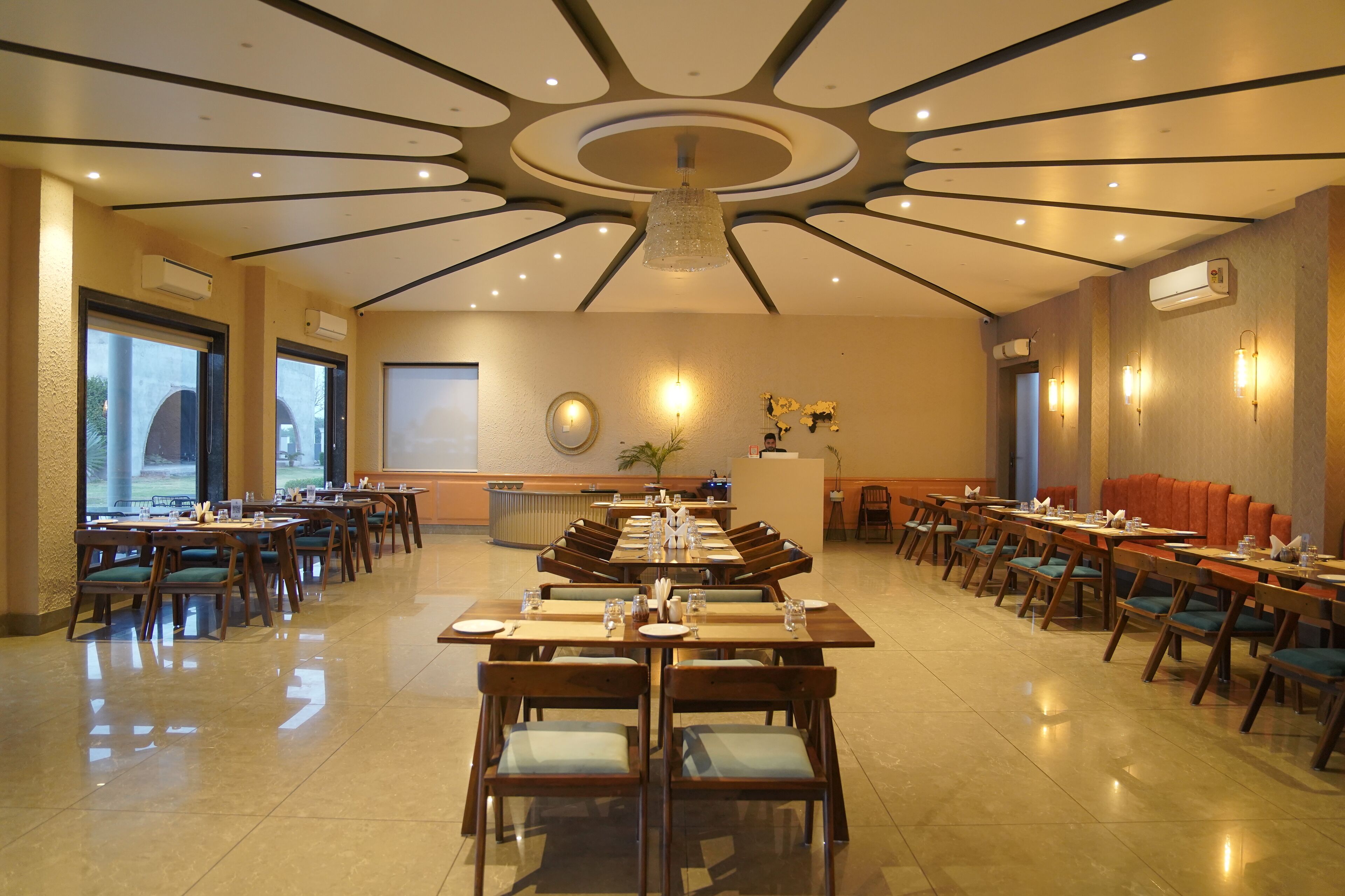 A spacious dining area with multiple tables and chairs, a central chandelier, and wall-mounted lighting.