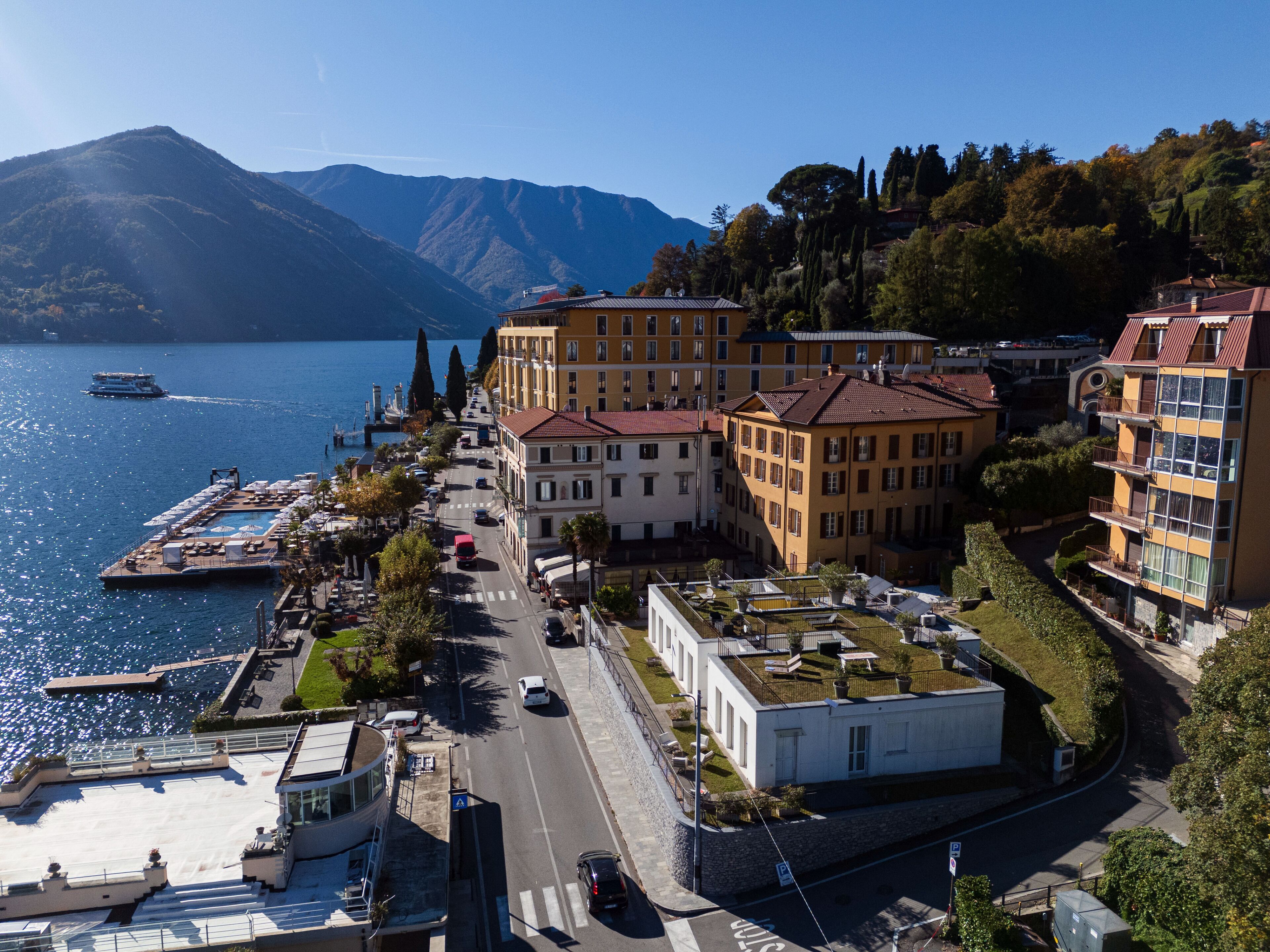 Una cittadina costiera con edifici lungo la banchina, un molo con imbarcazioni e una montagna sullo sfondo.
