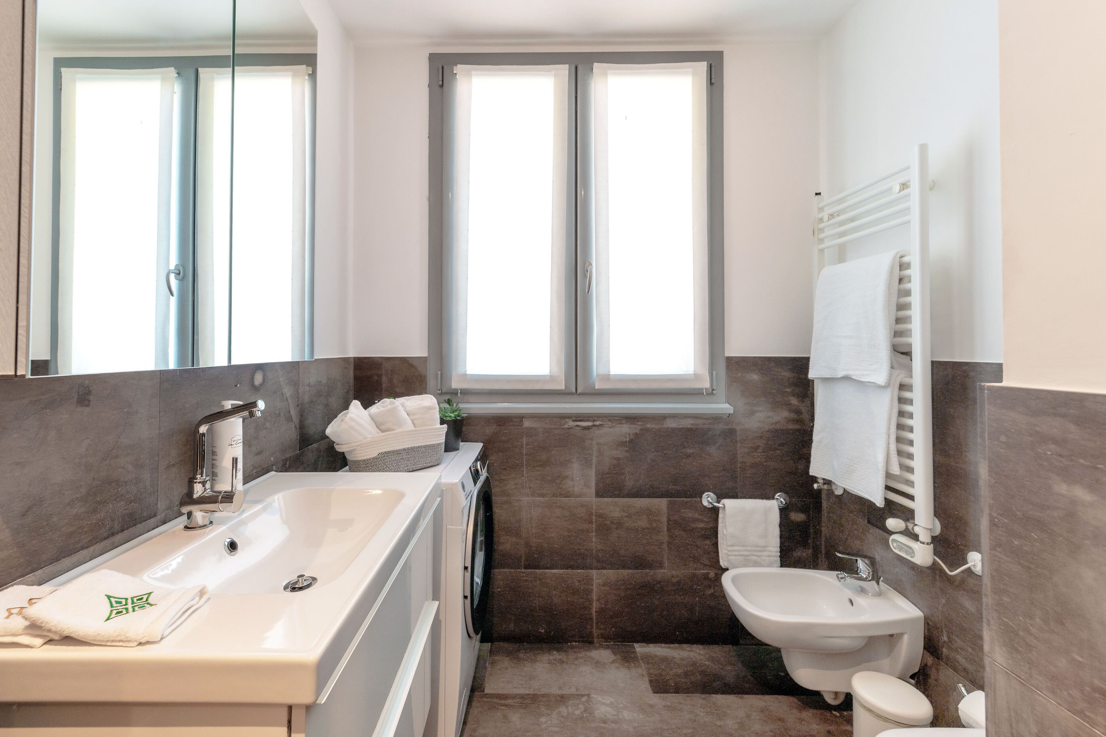 Een moderne badkamer met een ruime badkuip, een wastafel, een toilet en een raam voor natuurlijk licht.
