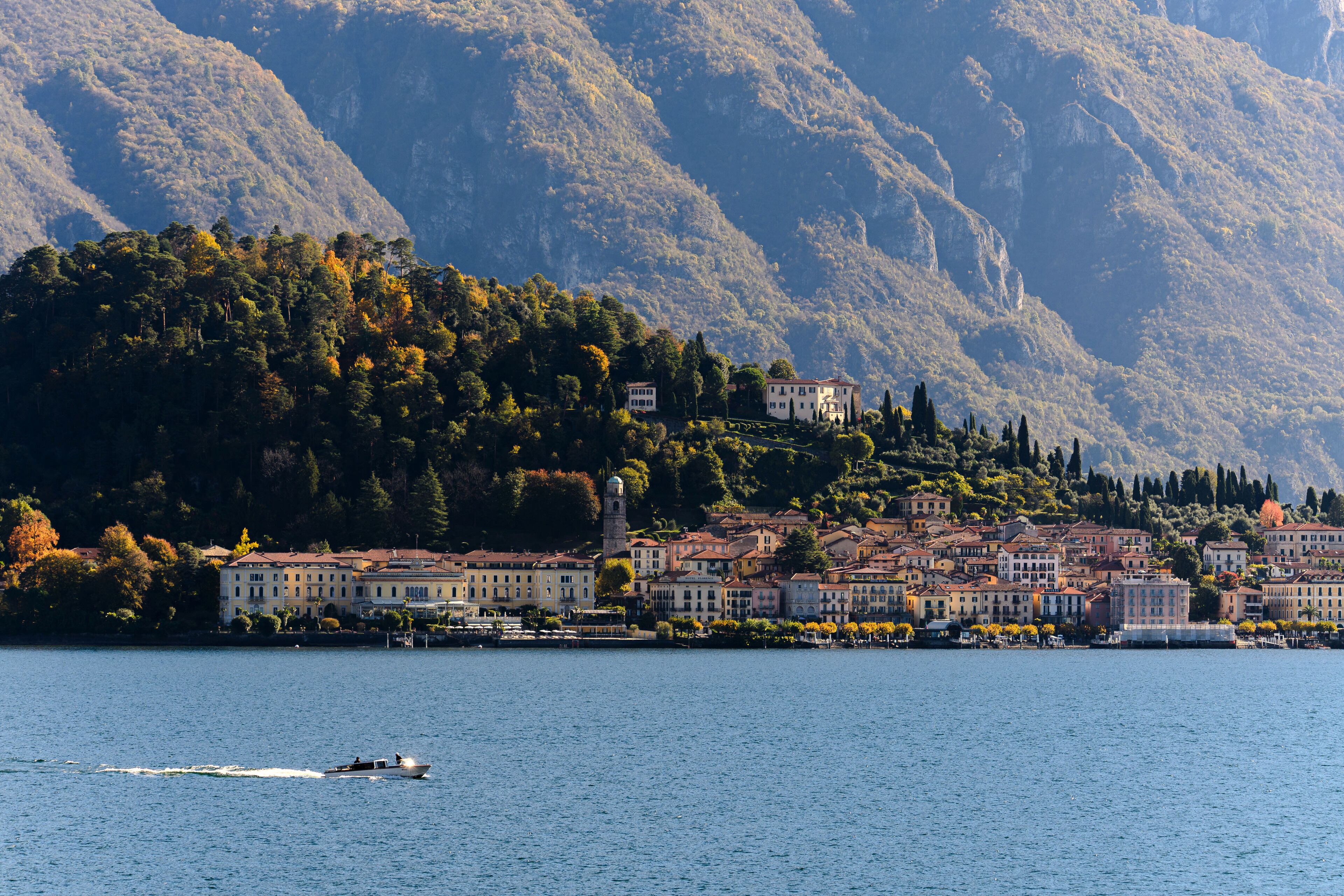 Eine Stadt am Seeufer mit Gebäuden am Ufer, ein Boot auf dem Wasser und Berge im Hintergrund.