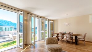 A spacious room with a large sliding glass door leading to a balcony with a mountain view. Inside, there is a dining area with wooden furniture and a patterned rug. - Residenza di Luce (Griante)