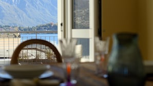 A dining table with a view of mountains and a lake through a window. - Residenza di Luce (Griante)