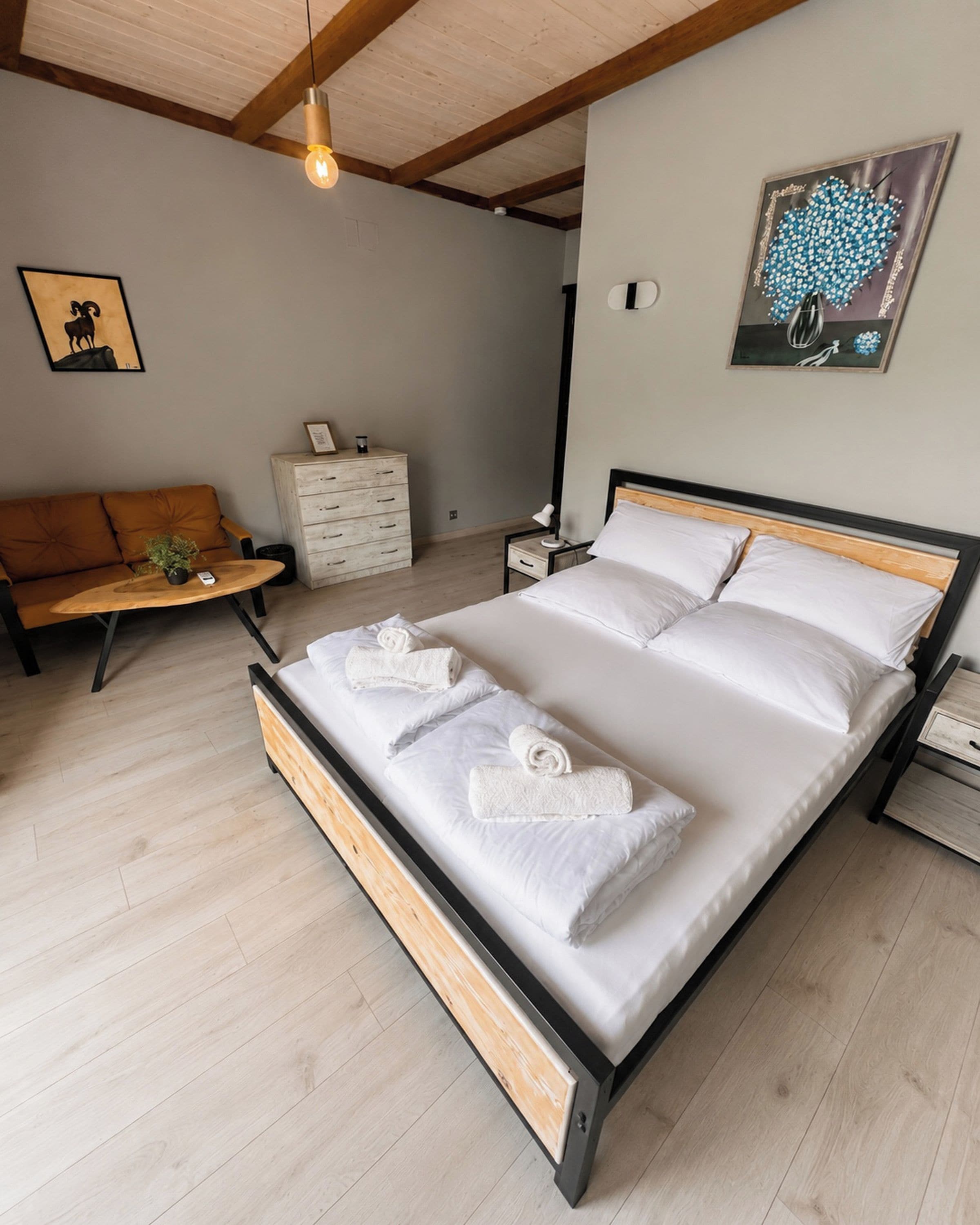 Een moderne slaapkamer met een houten bedframe, een houten vloer, een witte dressoir, een houten bankje en een wandlamp.