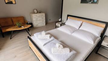 Een moderne slaapkamer met een houten bedframe, een houten vloer, een witte dressoir, een houten bankje en een wandlamp.