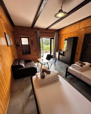 Una habitación con pared de ladrillo, vigas de madera en el techo, un sofá, una mesa de comedor con sillas, una cama y una pequeña kitchenette.