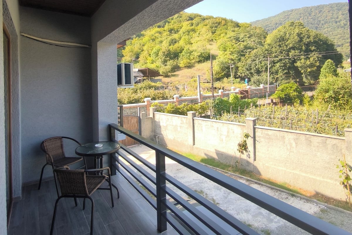 A balcony with a table and chairs, overlooking a hillside with a vineyard and a clear sky.