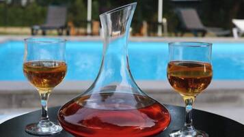 Escena junto a la piscina con una mesa que sostiene tres vasos con líquido color ámbar, probablemente una bebida, y una jarra de vidrio rojo.