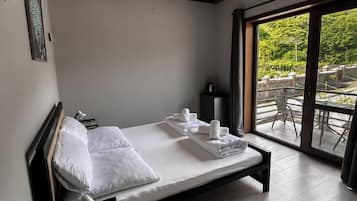 A modern bedroom with a wooden ceiling, a large bed with white linens, a bedside table, and a view of the outdoors through a glass door.