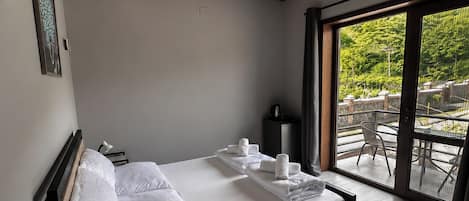 A modern bedroom with a wooden ceiling, a large bed with white linens, a bedside table, and a view of the outdoors through a glass door.