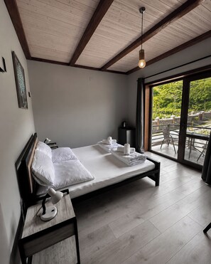 A modern bedroom with a wooden ceiling, a large bed with white linens, a bedside table, and a view of the outdoors through a glass door. - Arazani (Lagodekhi)
