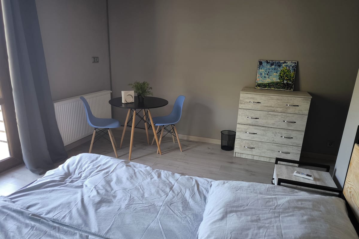 A bedroom with a bed, a small table with two chairs, a dresser, and a radiator.