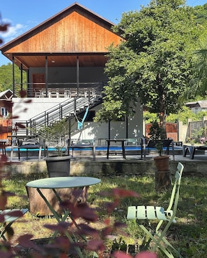 A wooden building with a staircase leading to a balcony, surrounded by greenery and outdoor seating. - Arazani (Lagodekhi)