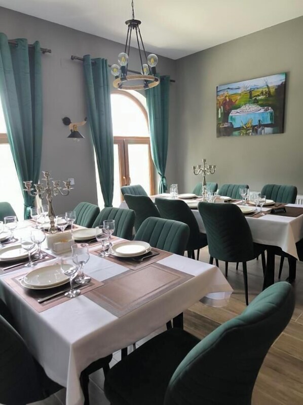 A dining area with tables set for a meal, green upholstered chairs, and a chandelier. - Arazani (Lagodekhi)