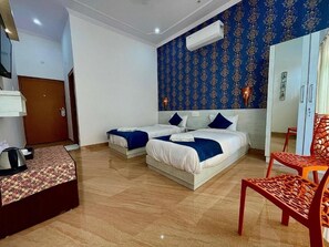 A hotel room with two beds, a wooden floor, a blue patterned wall, and a red chair. - Lacurcuma Luxury Homestay Khajuraho (Rajnagar)