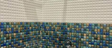 A shower with a square showerhead and a tiled wall with a mosaic pattern.