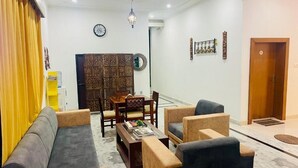 Een woonkamer met een zithoek, een salontafel en een eettafel met stoelen. Er is een decoratief paneel en een klok aan de muur.