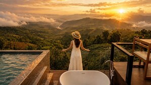 Donna con un vestito bianco e un cappello di paglia che ammira un paesaggio suggestivo, con vista sul tramonto, una piscina e un pontile in legno.