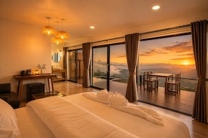 Une chambre d’hôtel avec un grand lit, un bureau, une chaise et une vue sur le coucher de soleil par la fenêtre.