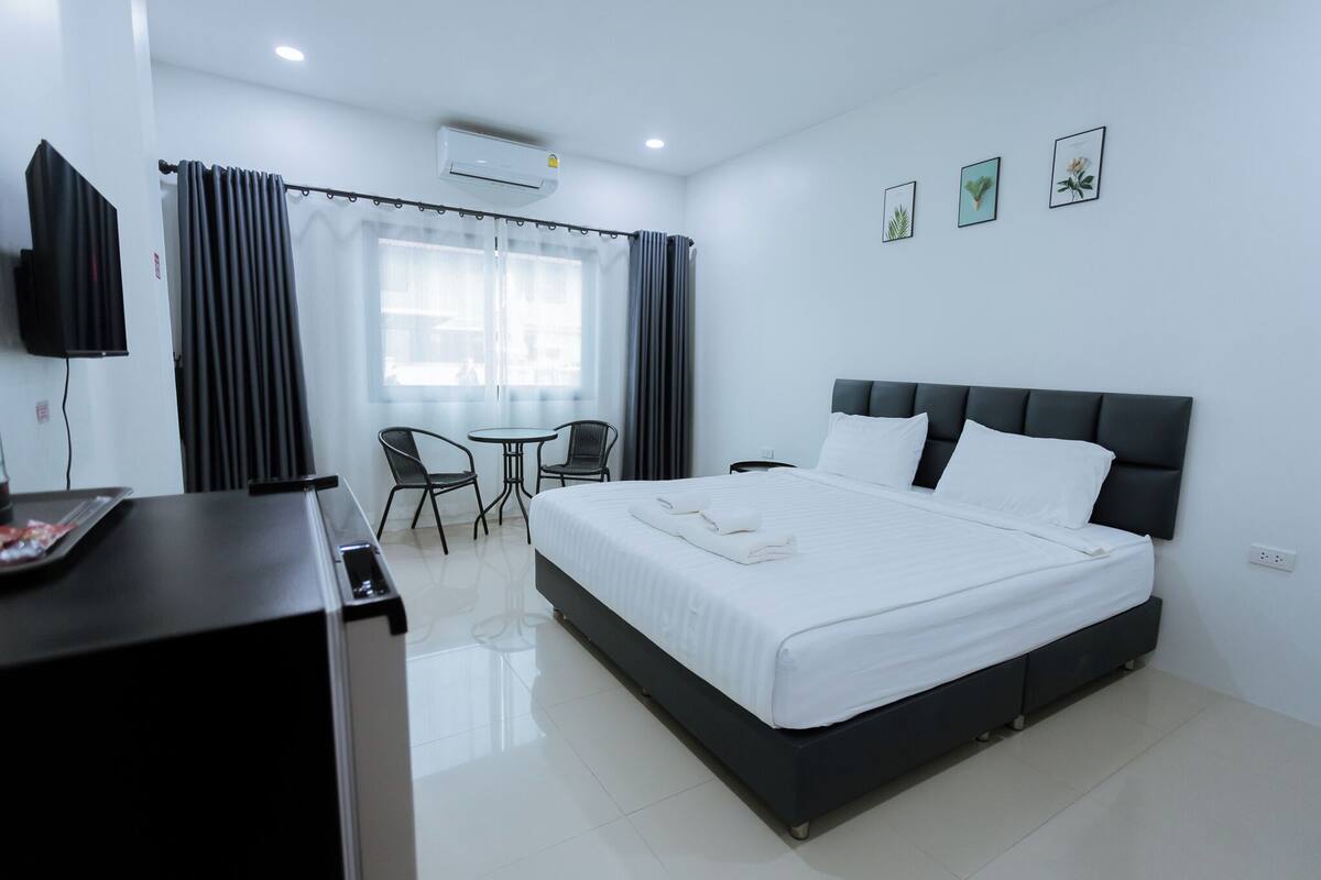 A hotel room with a bed, a desk, a chair, a TV, and a window with curtains.
