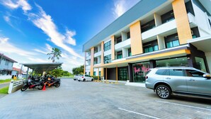 A modern building with a covered parking area, a restaurant named "The Kick," and several parked vehicles. - The Rich Hotel (Surin)