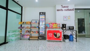 A room with a refrigerator stocked with beverages, a vending machine, and a table with a microwave and a kettle. - The Rich Hotel (Surin)