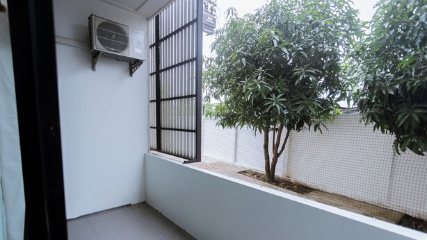 A small balcony with a tiled floor, a black metal gate, and a tree. - The Rich Hotel (Surin)