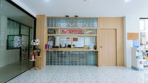 A reception desk with a 'RECEPTION' sign, a glass display case, and a wooden counter. - The Rich Hotel (Surin)