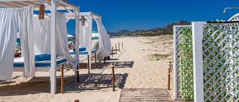 Een strandgebied met witte parasols, een houten terras en een wit lattenhek.